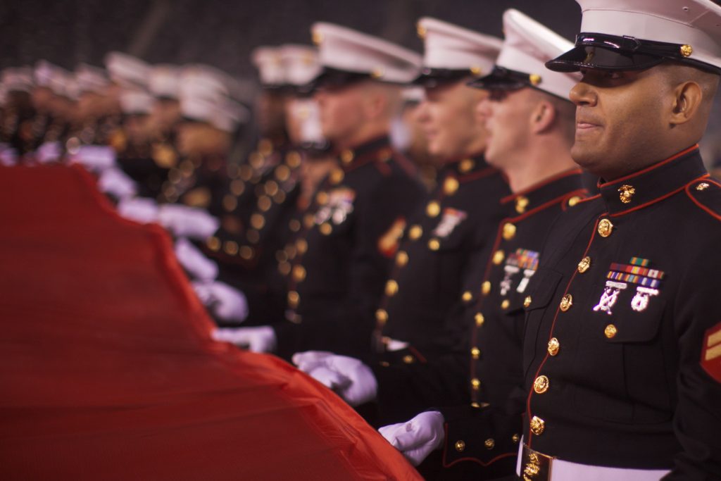 Soldados, pilotos de las fuerzas aéreas y marines desenrollan una bandera estadounidense en una ceremonia de apreciación del ejército en un partido de los New York Jets contra los New England Patriots el 13 de noviembre de 2011, Sargento Sandall A. Clinton/Flickr